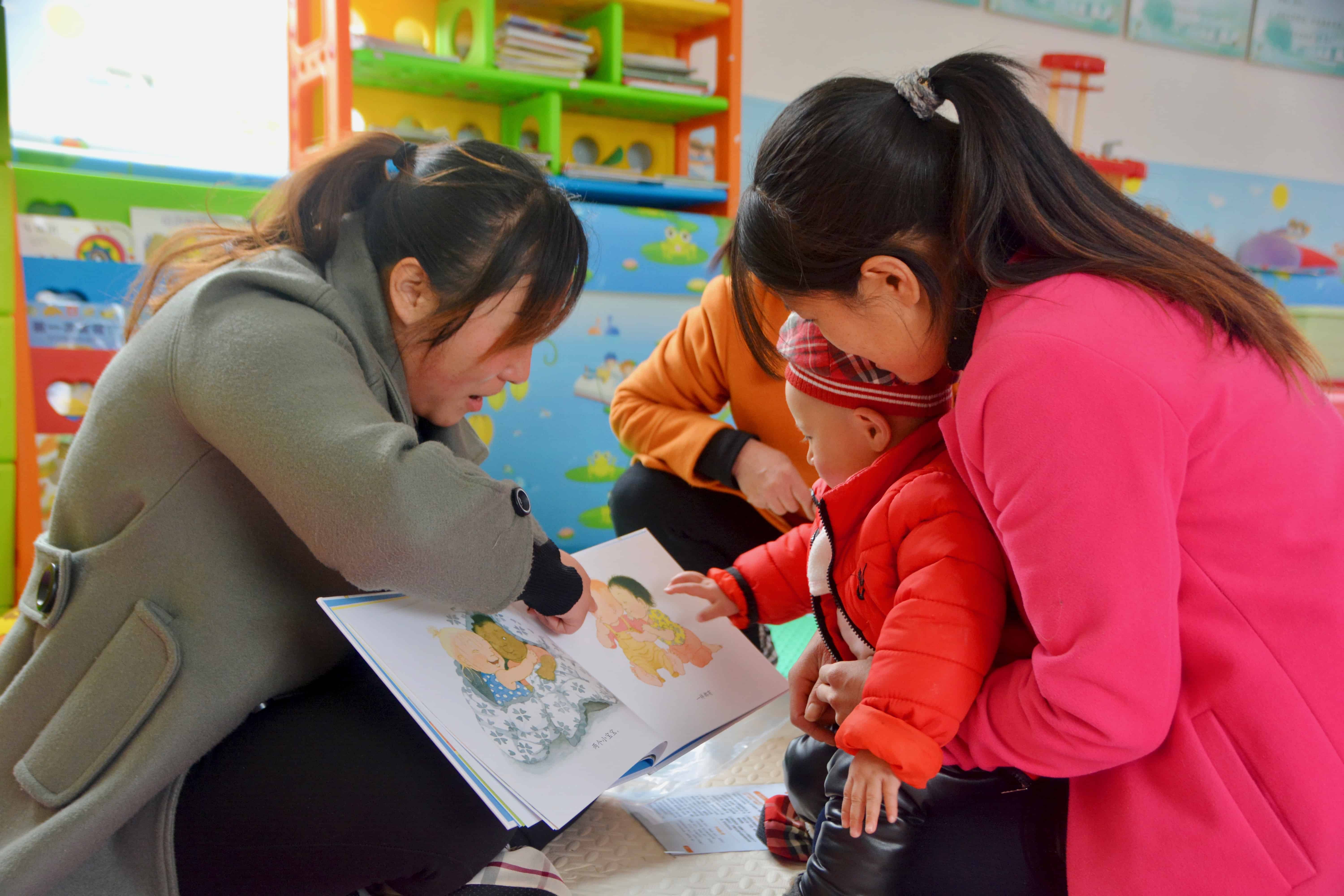 A baby reading with two adults