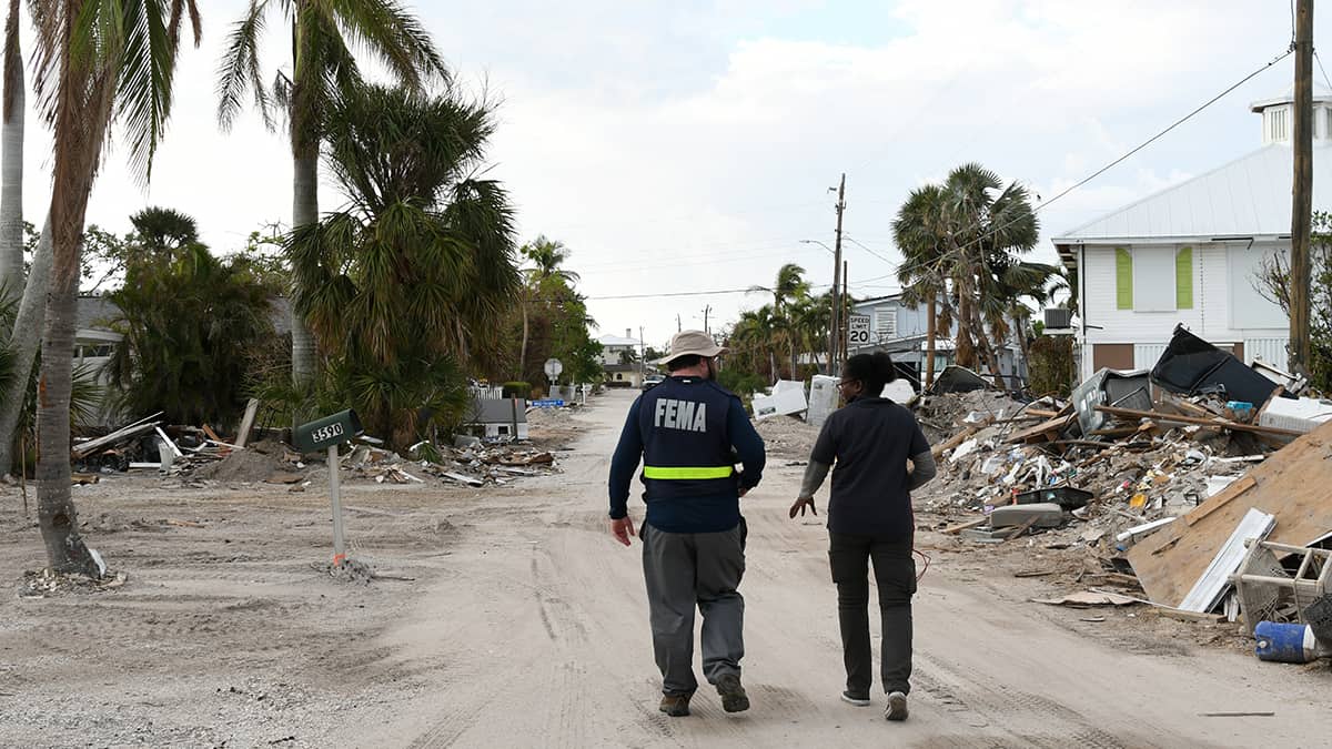 In Fort Myers, Florida, two FEMA disaster survivor assistant team members walk by damaged houses and rubble as they canvas a neighborhood hit by Hurricane Ian. (Jocelyn Augustino/FEMA)